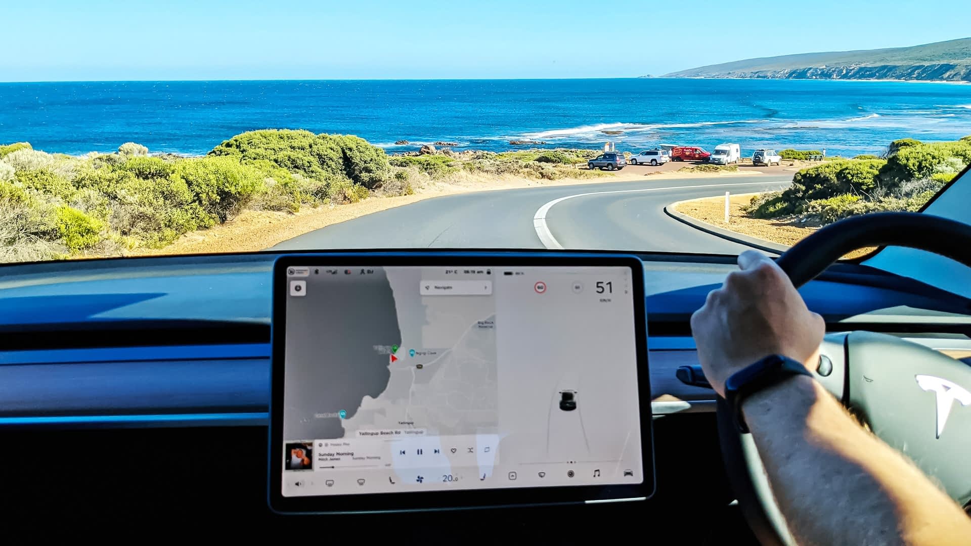 Tesla Model 3 driving down winding beach road